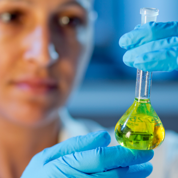 A woman with blue gloves holds up a glass tube with green liquid.